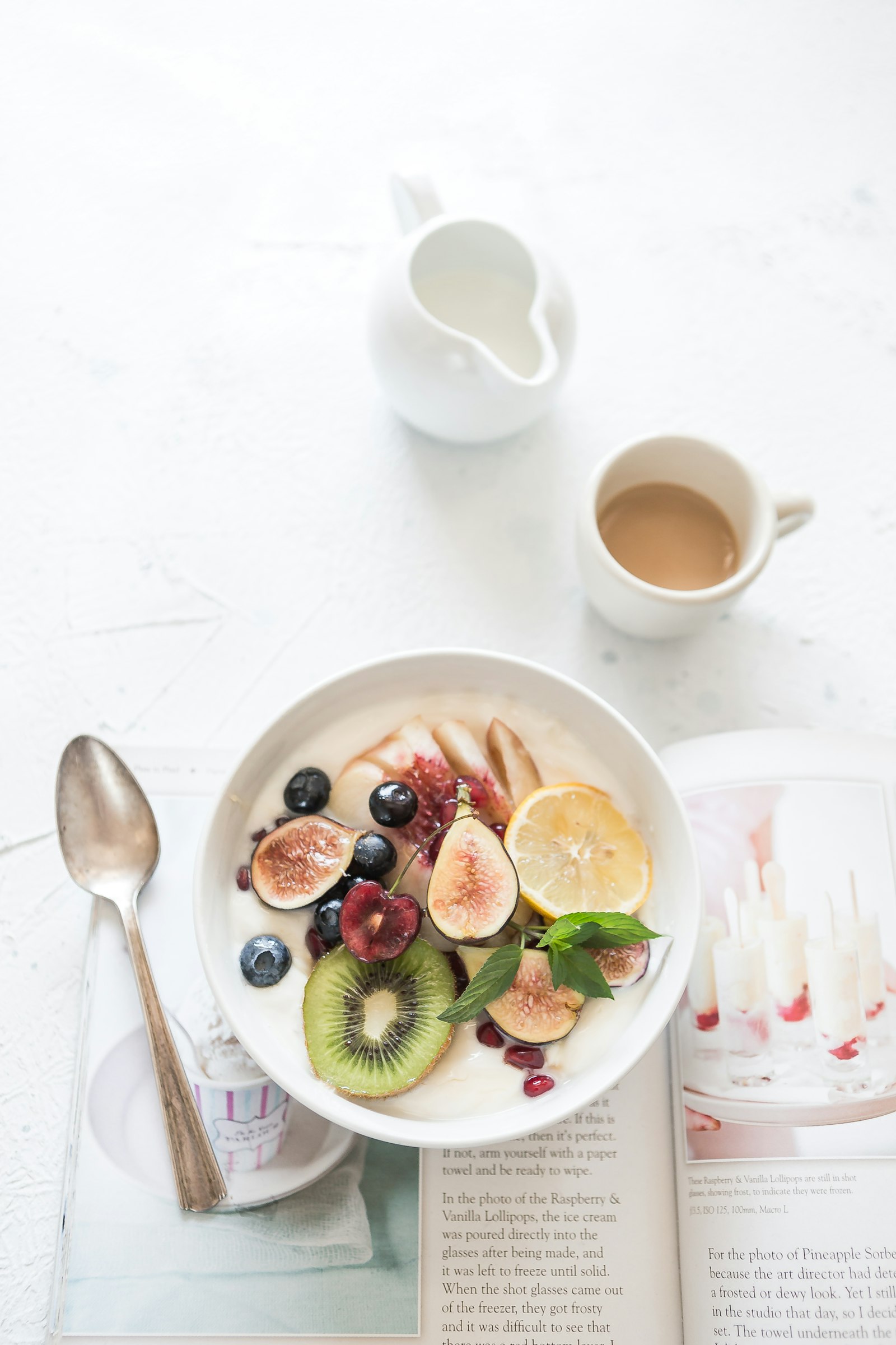 A bowl of yogurt topped with fruit beside a cup of coffee on a table