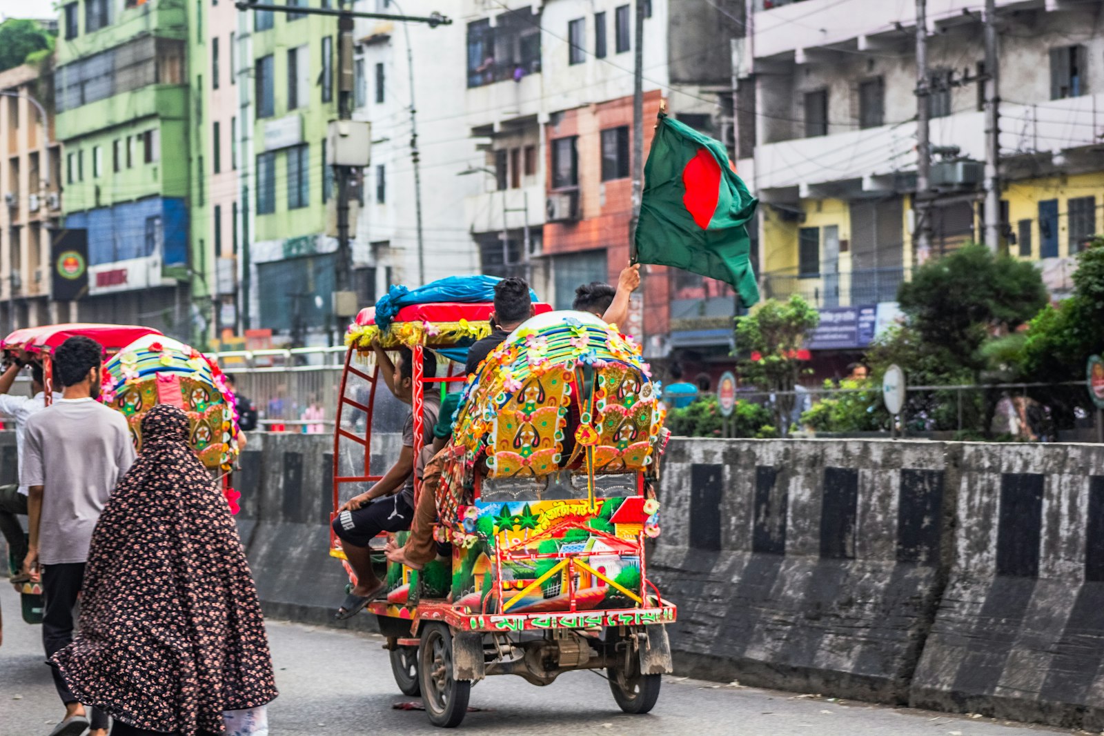A colourful cycle-rickshaw and pedestrians on a busy South Asian city street