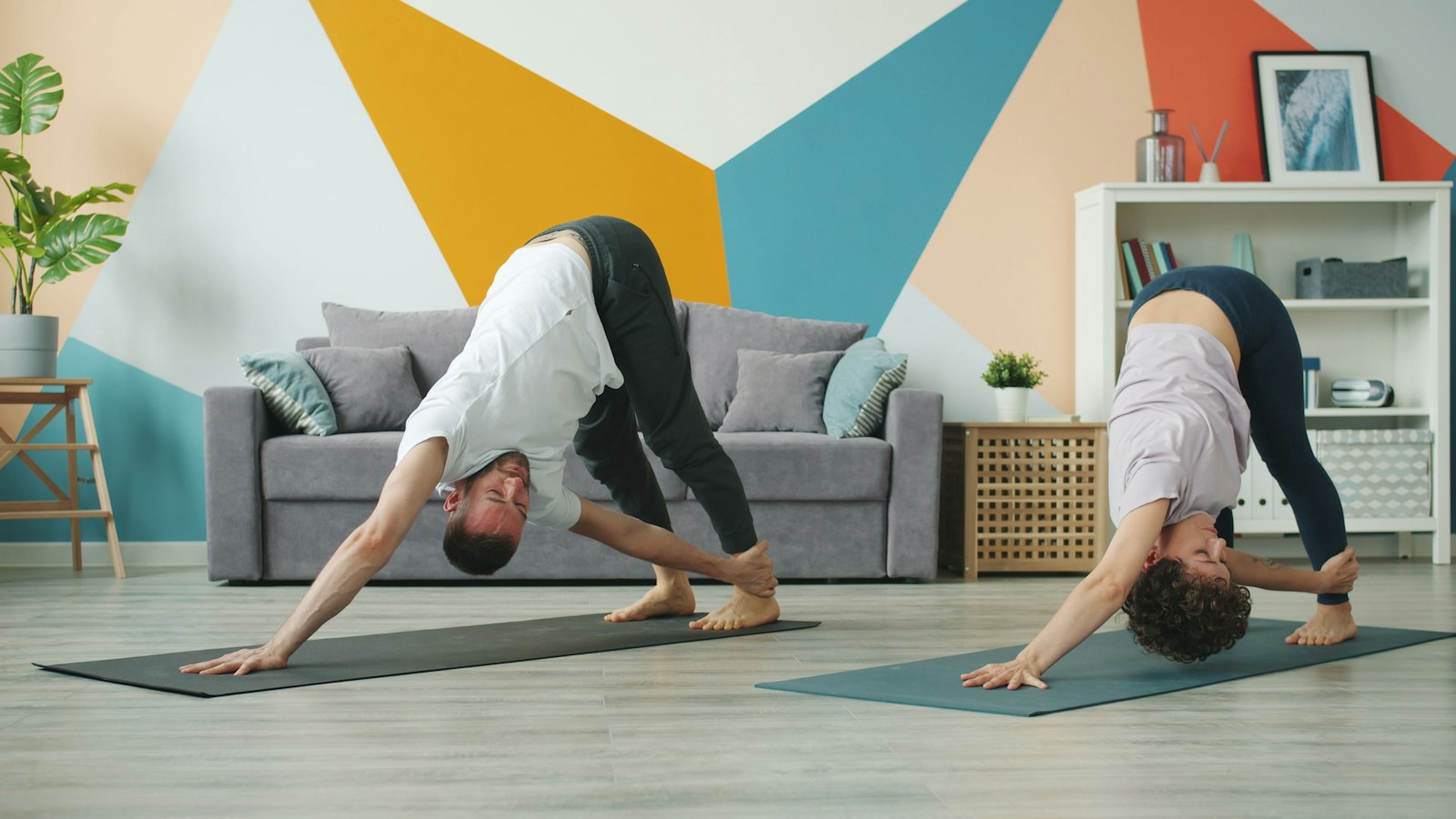 A couple practising yoga stretches on mats in a living room