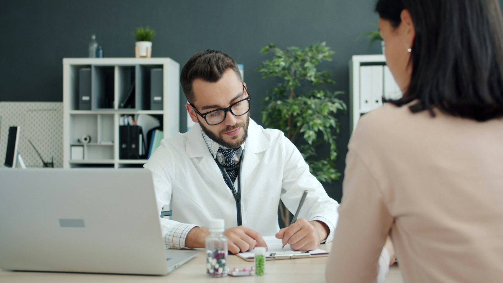 A doctor writing notes while speaking with a patient across a desk
