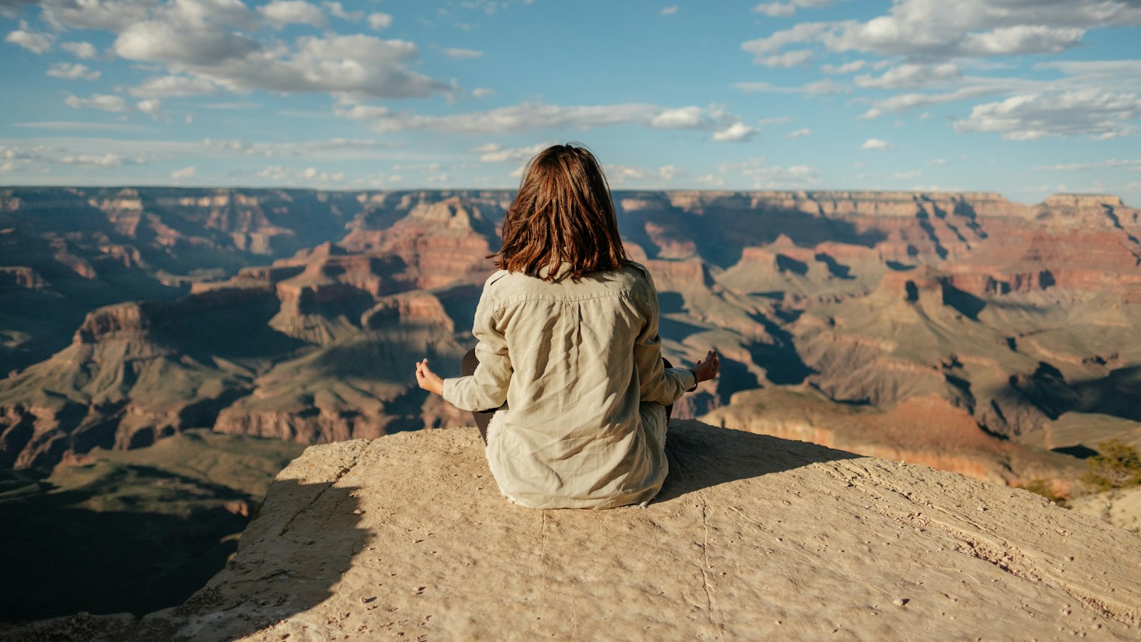 A person in a light shirt sitting quietly on a rocky ledge overlooking a wide valley