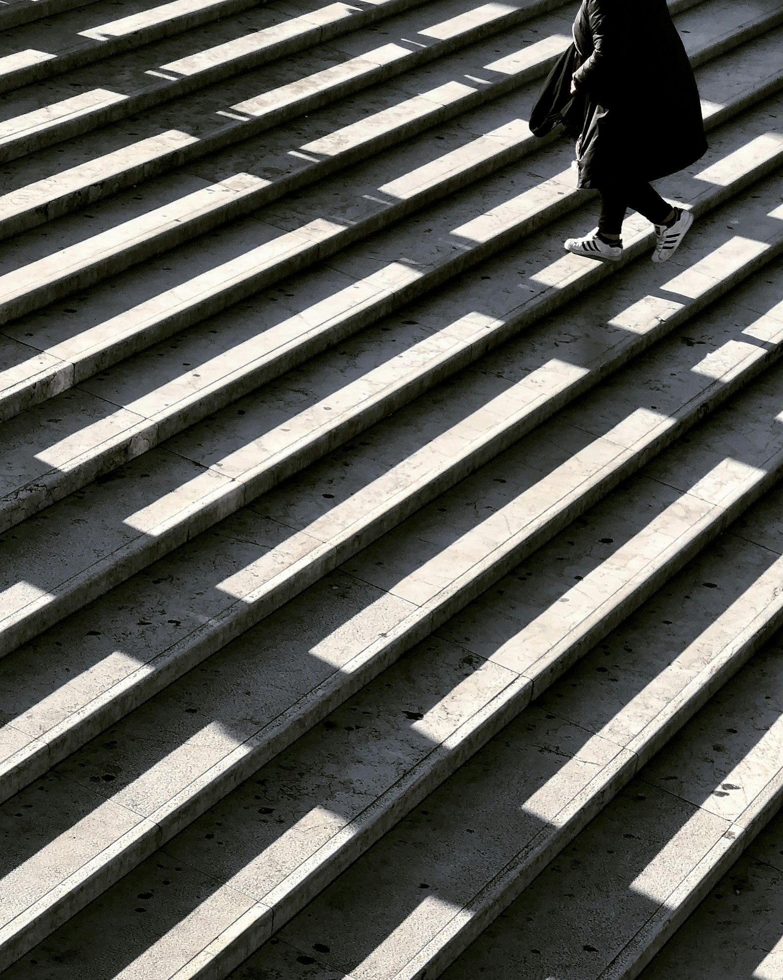 A person walking up a long flight of outdoor concrete stairs