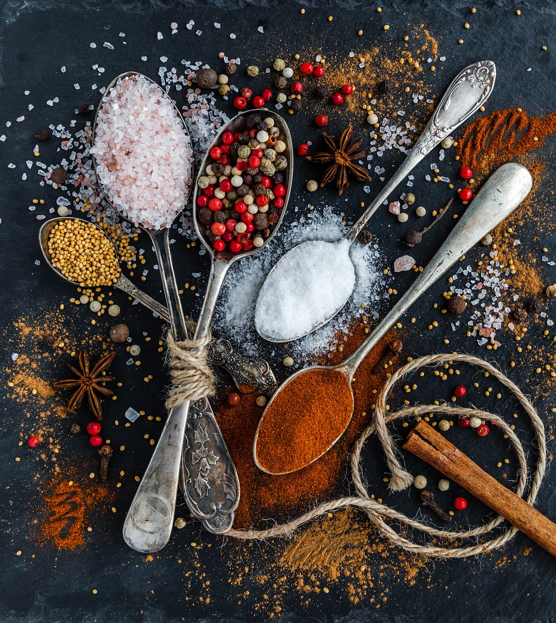 Spoons and bowls filled with colourful ground spices on a dark table