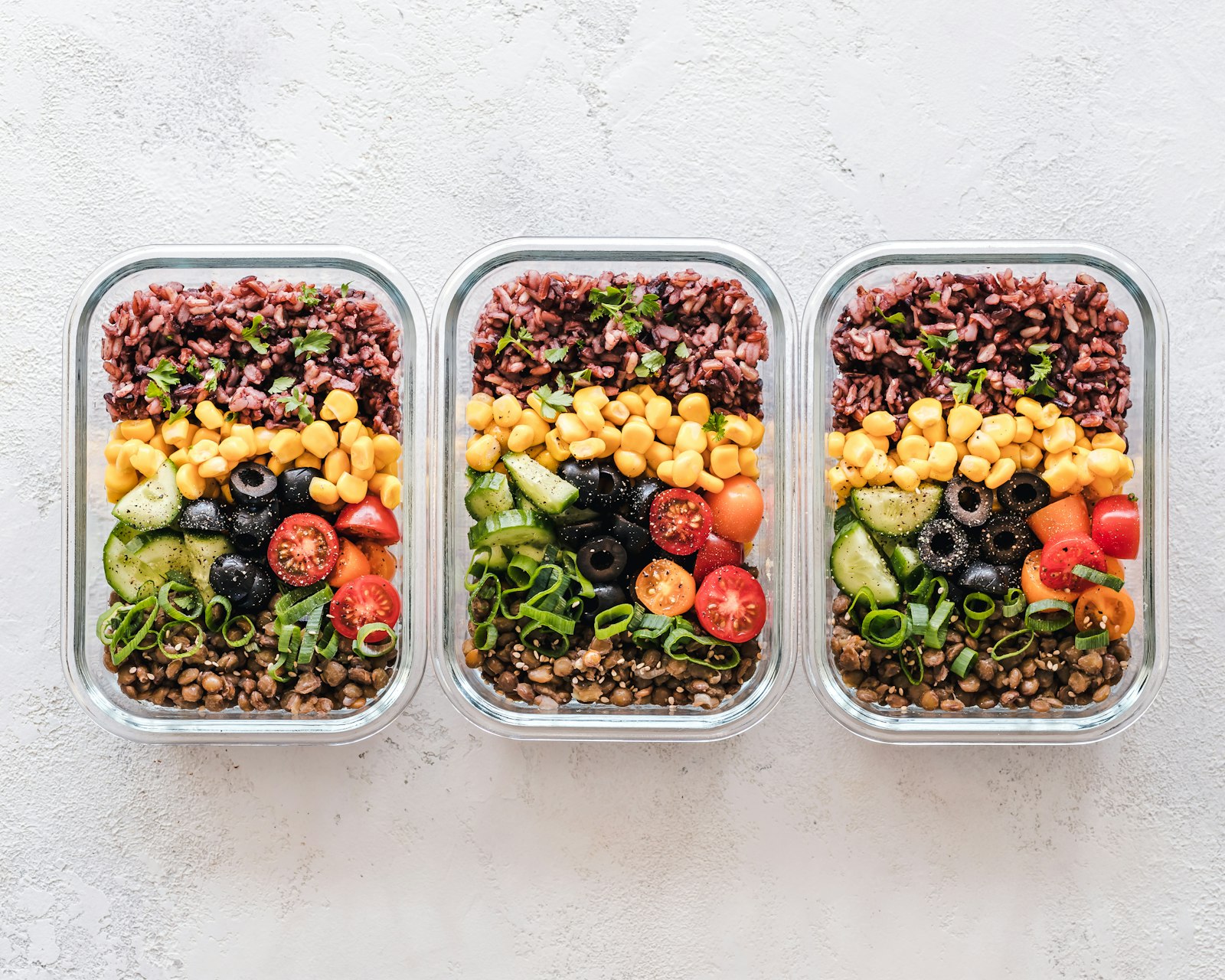 Three glass meal-prep containers filled with rice, vegetables and salad