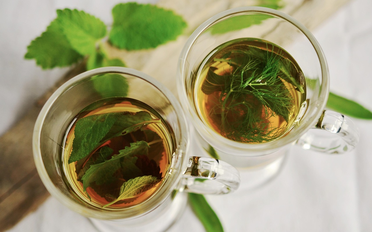 Two glass cups of herbal tea beside fresh mint and tea leaves