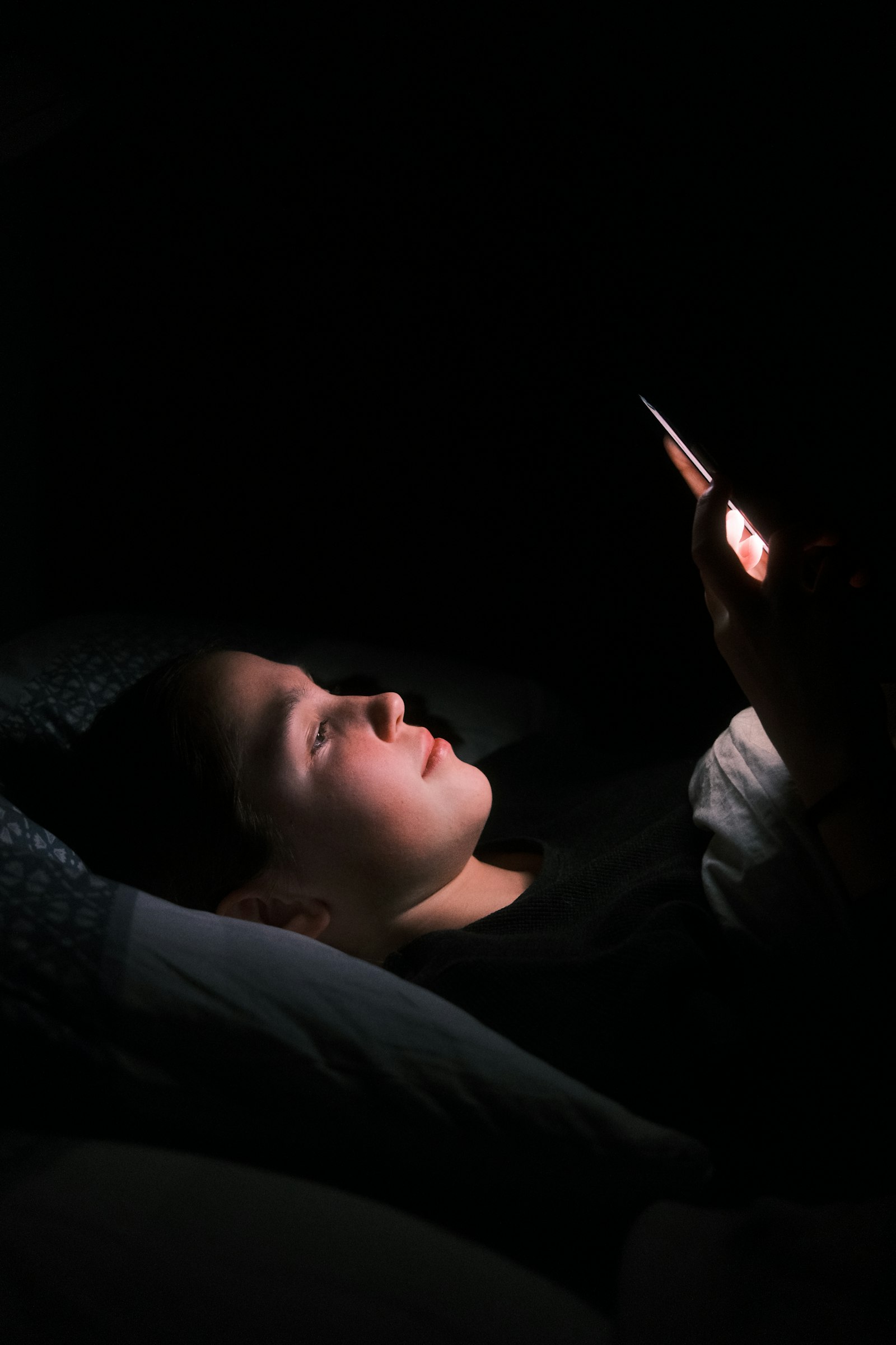 A woman lying in bed at night lit by the glow of her phone
