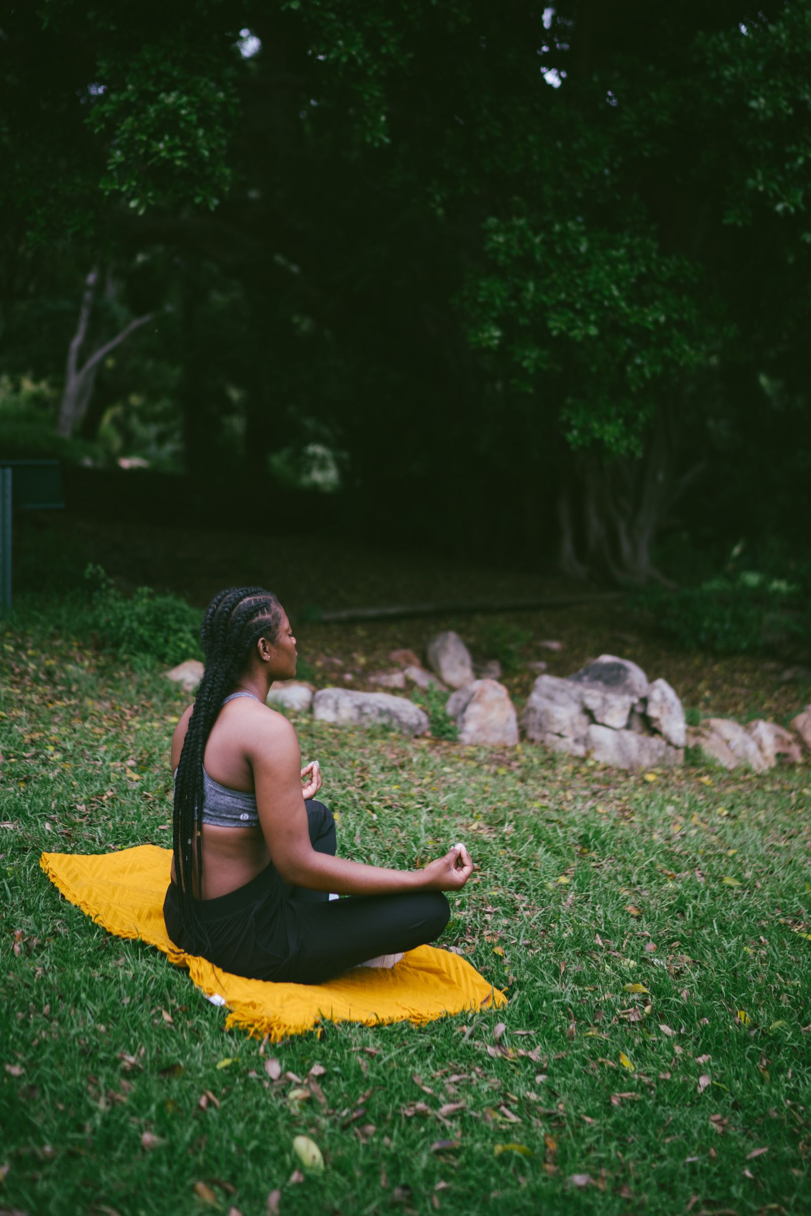 A woman meditating outdoors on a mat surrounded by greenery