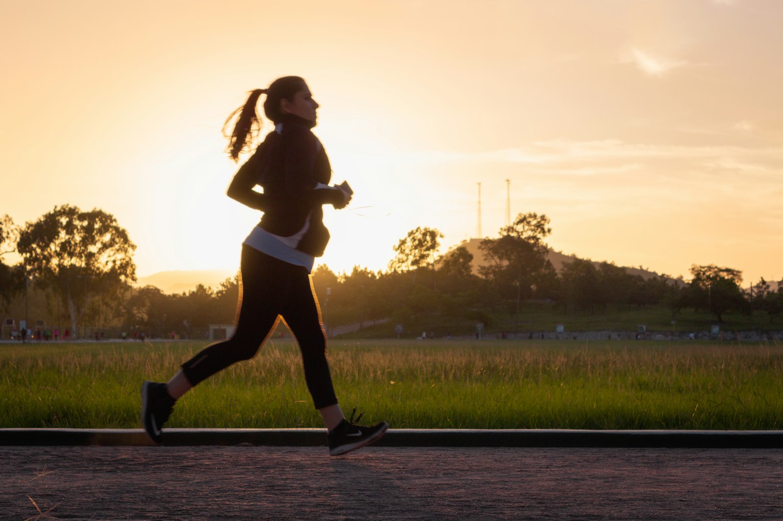 A woman running along a path at sunrise, silhouetted against golden light
