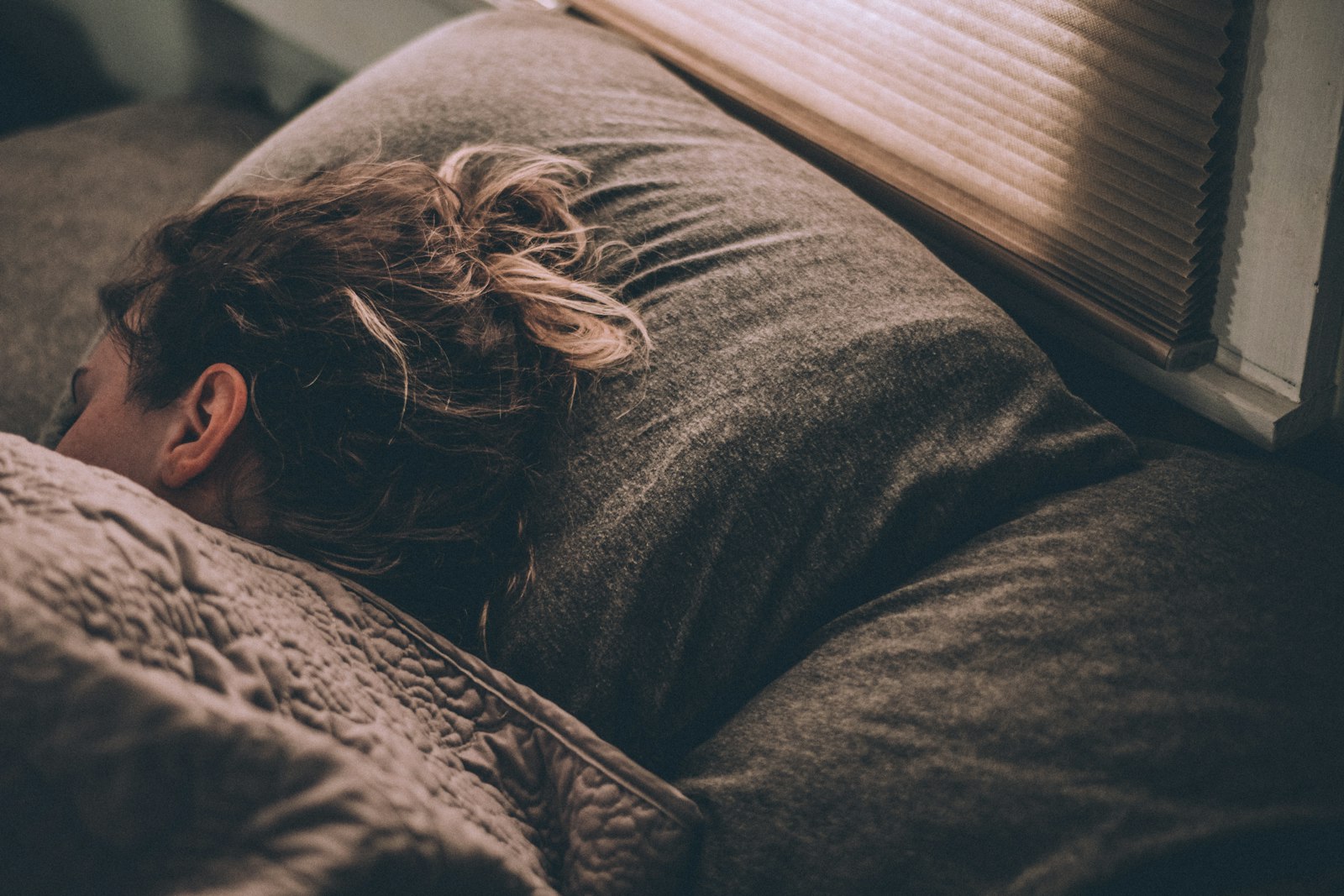 A woman sleeping under soft blankets in a dim bedroom